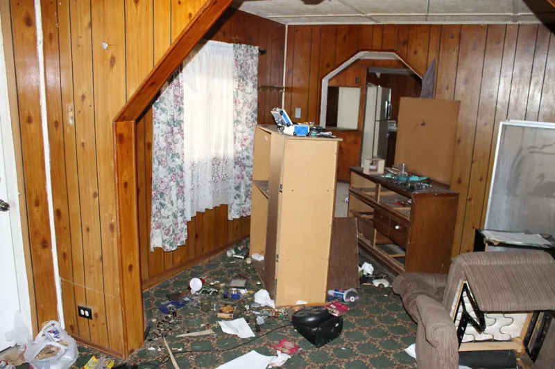 Foreclosure trash out, before: broken furniture, trash and debris left across a paneled living room