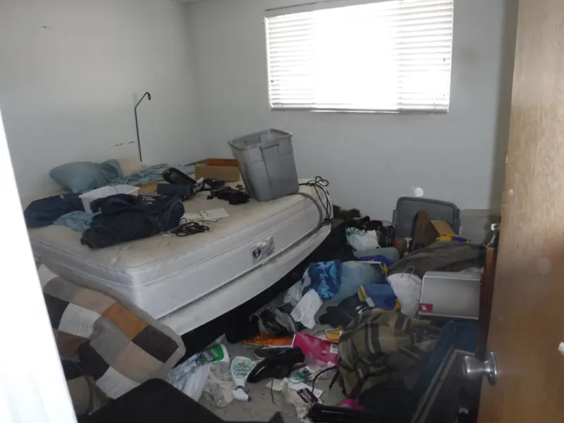REO trash out, before: a mattress, storage bins, clothes and trash left in a bedroom