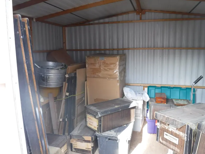 Shed clean out before: boxes, bins and furniture packed inside a metal shed