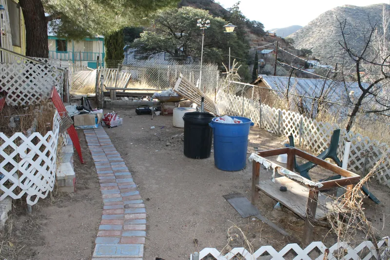Storm debris cleanup, before: broken lattice fencing, trash cans and scattered debris in a dirt yard